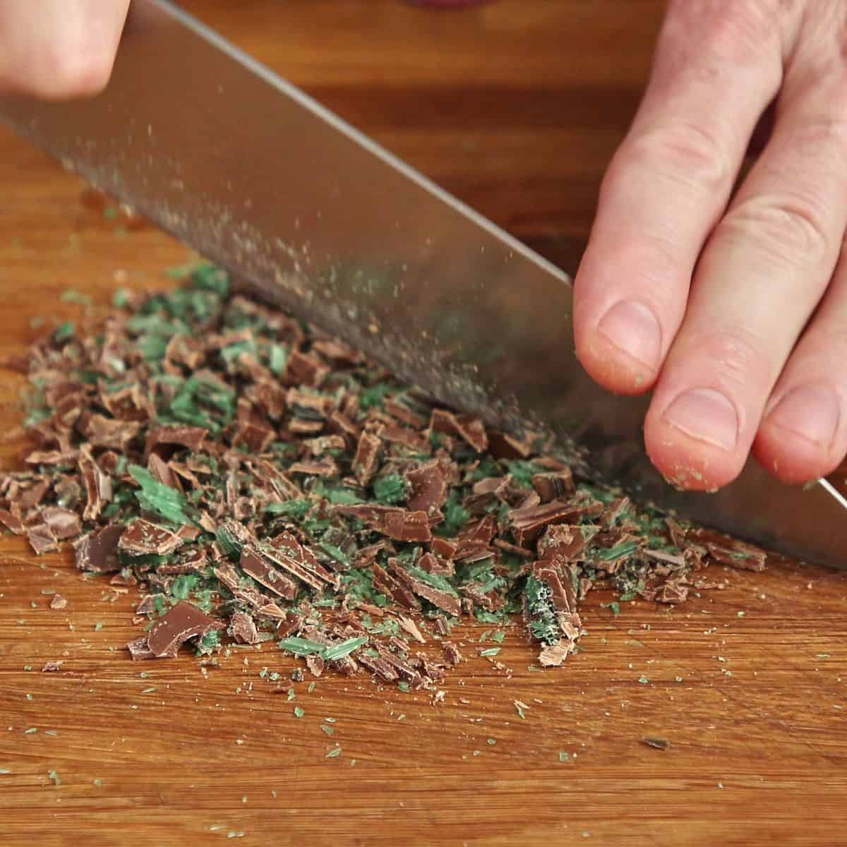 Peppermint Crisp chocolate frozen and being chopped into fine clean shards on cutting board.