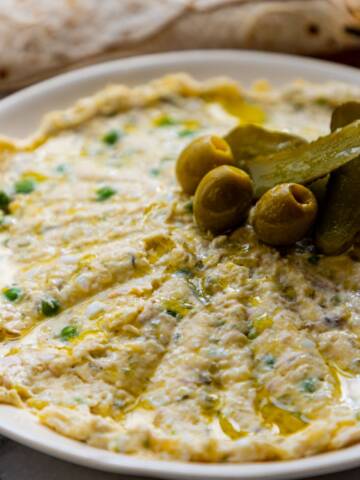 Persian olivieh salad with chicken served on a white plate with pickles, olives and flat bread.