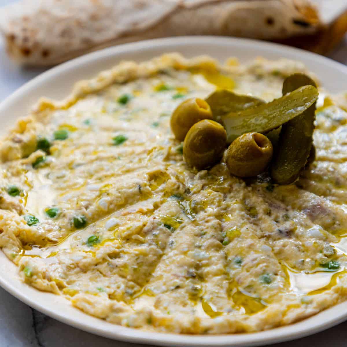 Persian olivieh salad with chicken served on a white plate with pickles, olives and flat bread.