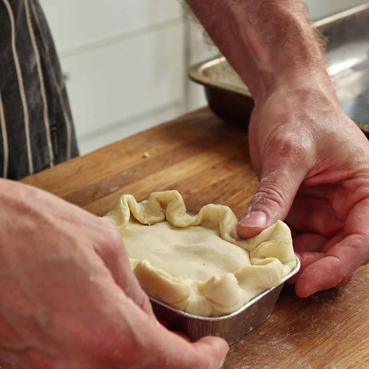 Pie edges being crimped with fork tines pressed down around outside creating sealed pattern