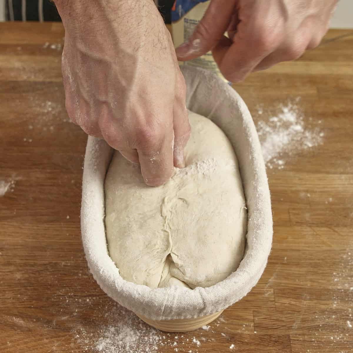 Hands pinching the seam close on sourdough bread inside a proving basket.