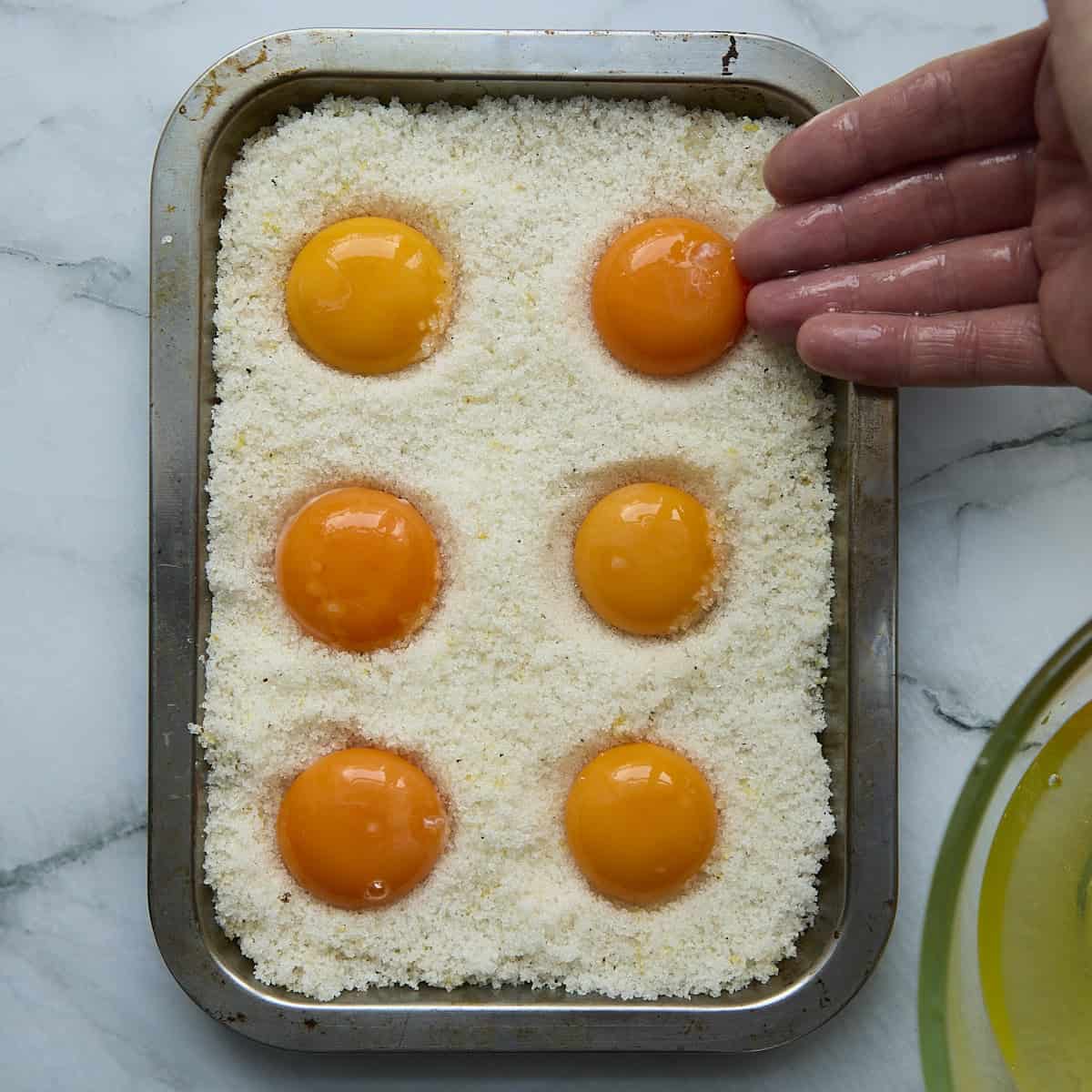Placing egg yolks into salt cure by hand.