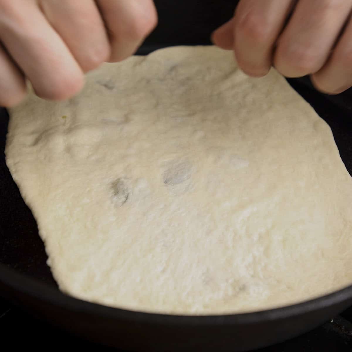 Placing naan into hot black skillet.