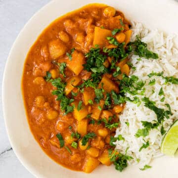 Potato chickpea and coconut curry with rice and lime in a white bowl.