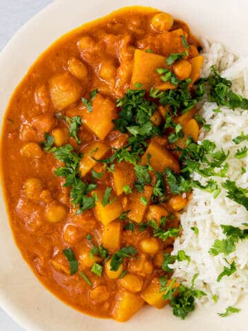 Potato chickpea and coconut curry with rice and lime in a white bowl.