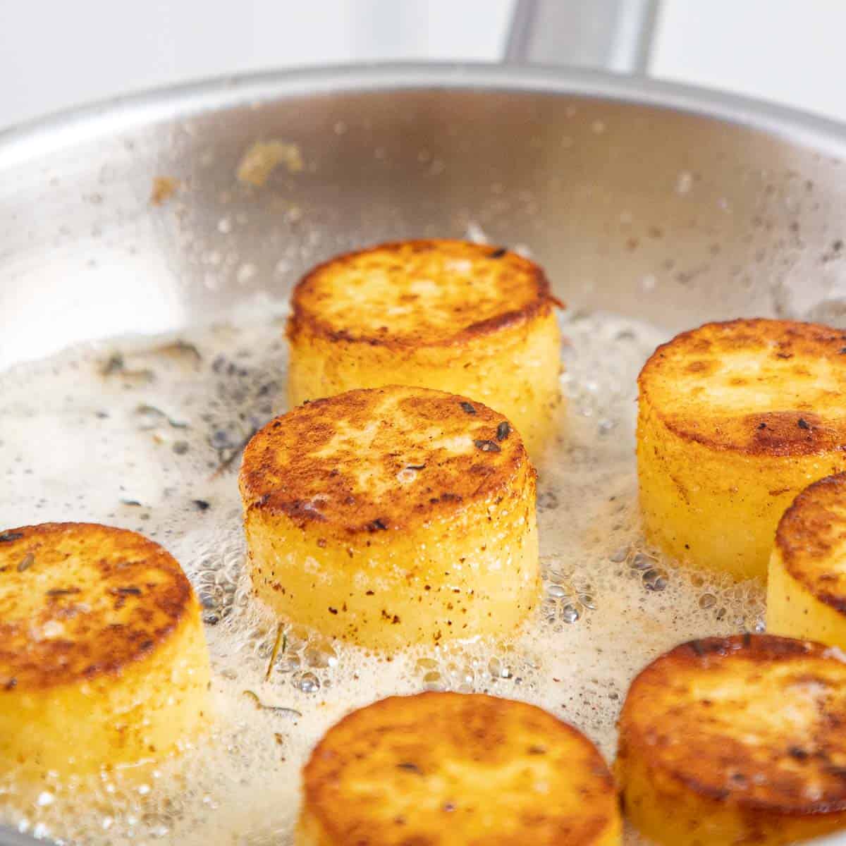 Potato cylinders in a frying pan with butter.