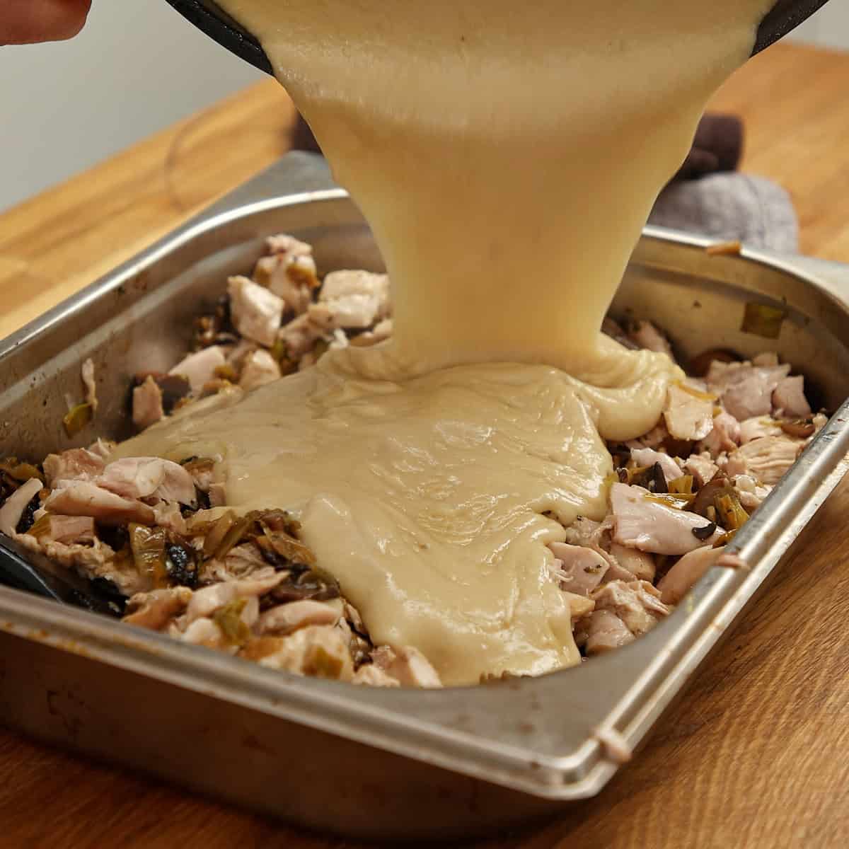 Smooth velouté poured over shredded chicken and vegetables in a tray.
