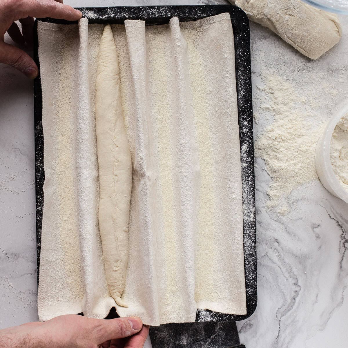 Placing baguettes onto a floured couche on a black tray.