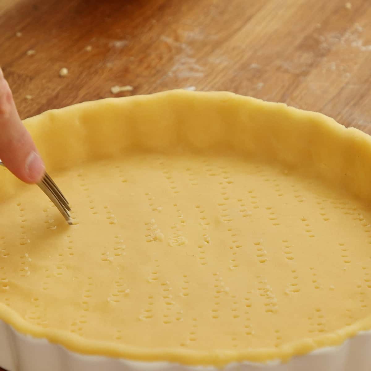 Shortcrust pastry shell being pricked with a fork before baking.
