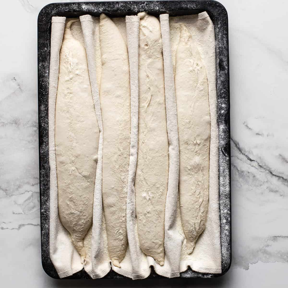 Proven baguettes on a black tray.
