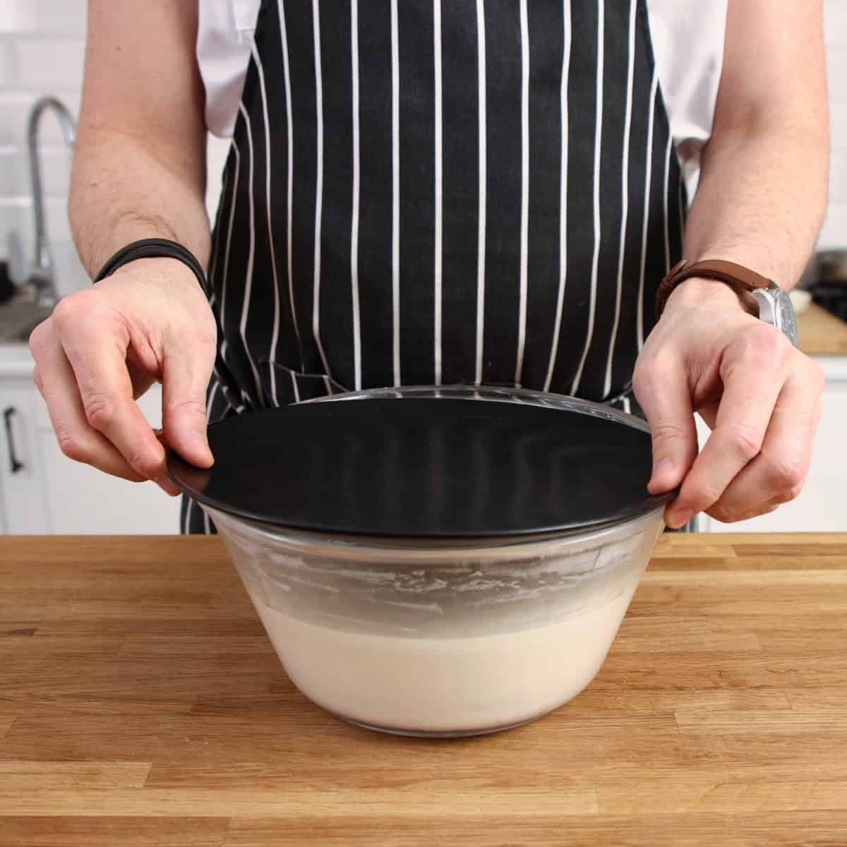 Dough in a bowl closed with a black plate.