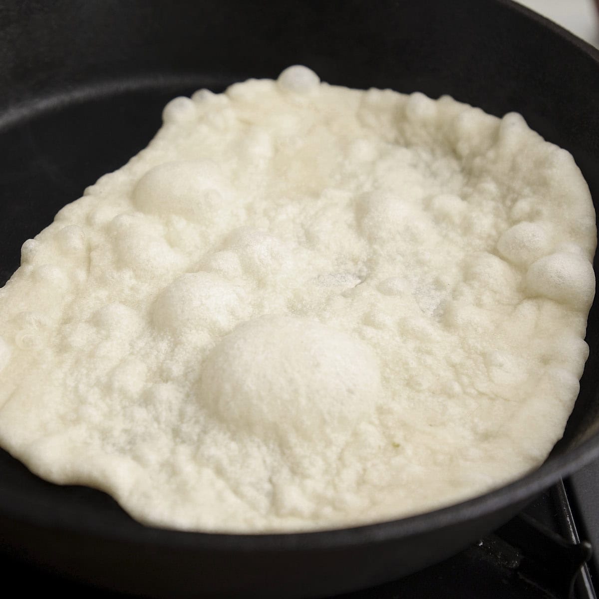 Puffing naan bread in a black skillet.