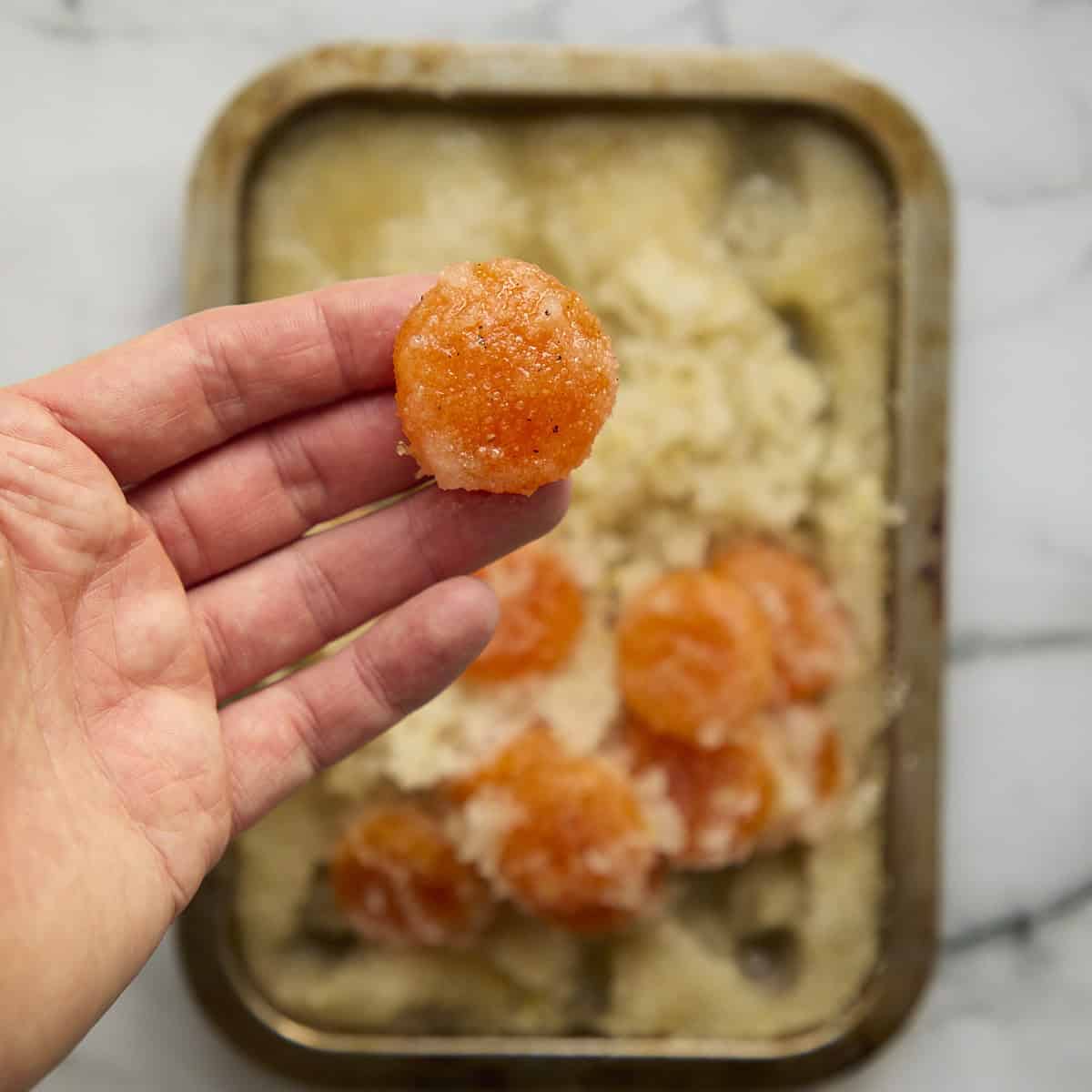Cured egg yolk in hand with cure mixture on it.