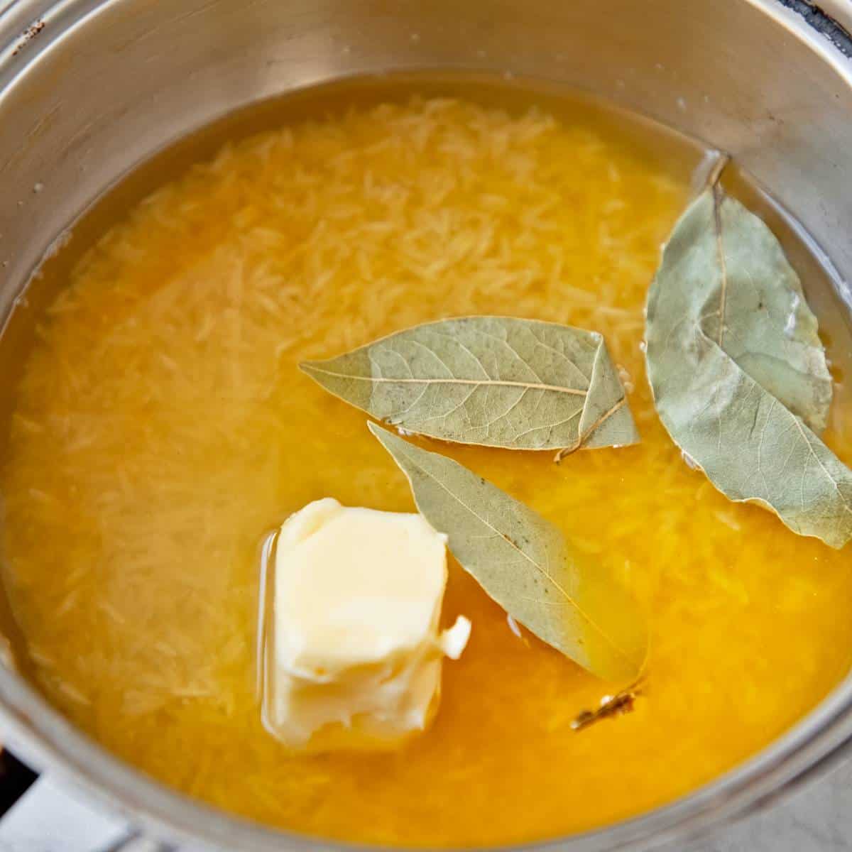 Rice with stock, aromatics, and butter in a pan.