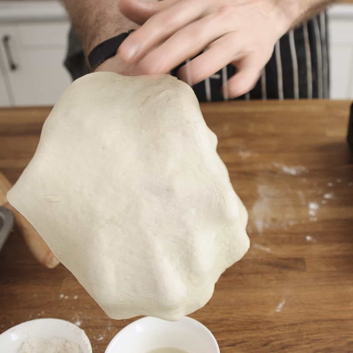 Rolled out naan stretched over a hand.