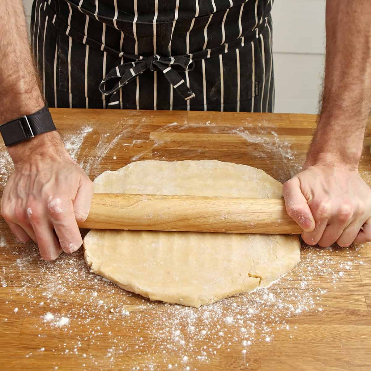 Shortcrust pastry being rolled thin with a wooden pin on a floured board.