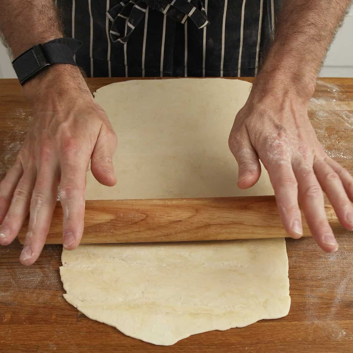 Rolling pastry out on a wooden surface with a rolling pin.