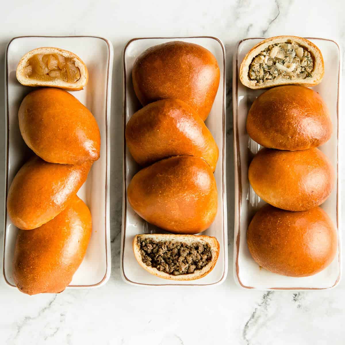 Individual apple, meat and cabbage Russian piroshki on marble background.