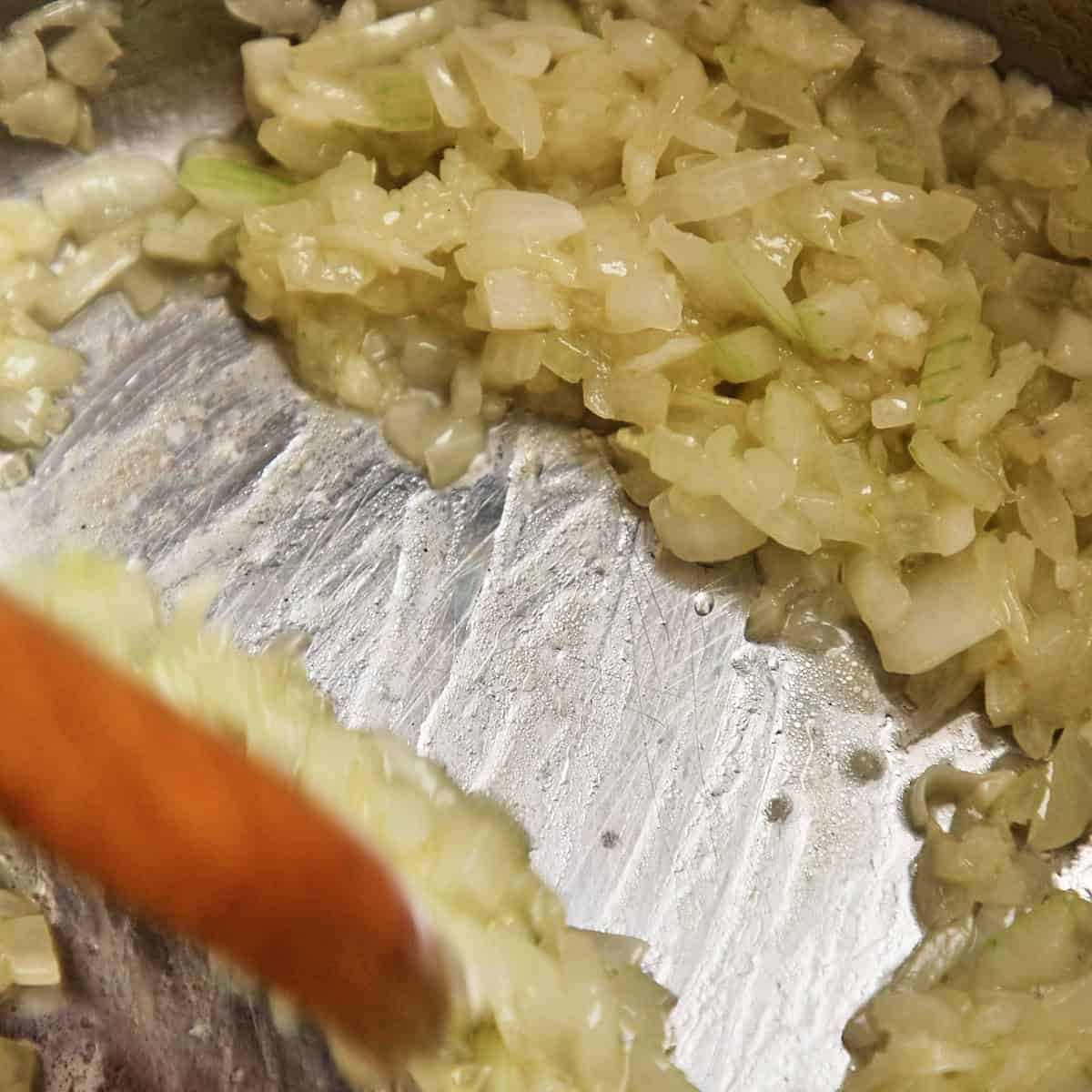 Diced onions and garlic sweating in a pot with a wooden spoon.