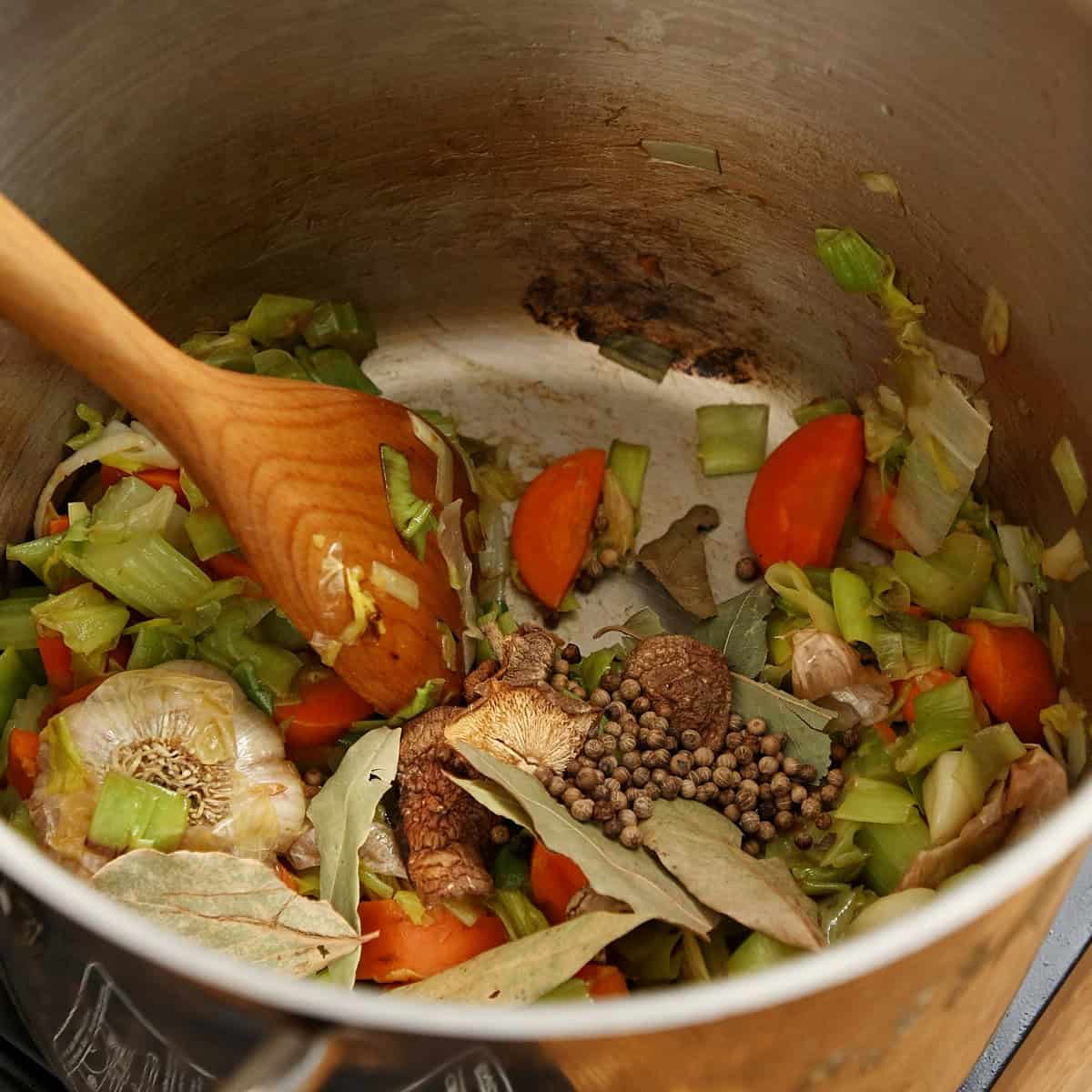 Leek, carrot, garlic, peppercorns, and bay leaves cooking in a heavy pot.