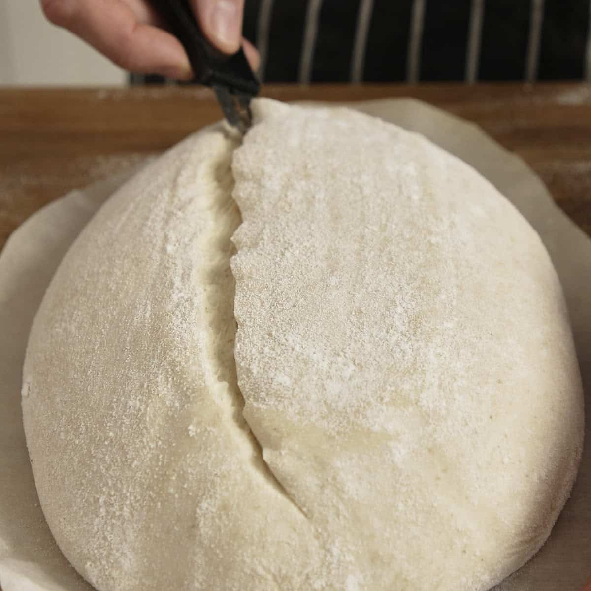 Razor blade scoring the top of a sourdough loaf before baking.