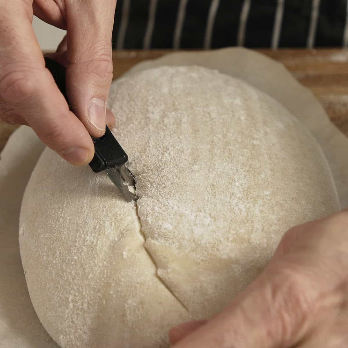 Razor blade scoring the top of a sourdough loaf before baking.