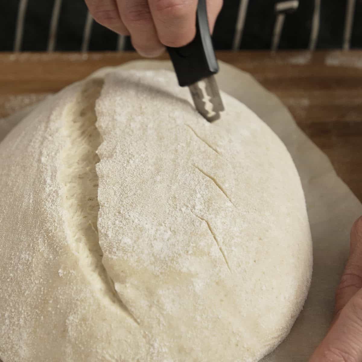 Razor blade scoring the top of a sourdough loaf before baking.