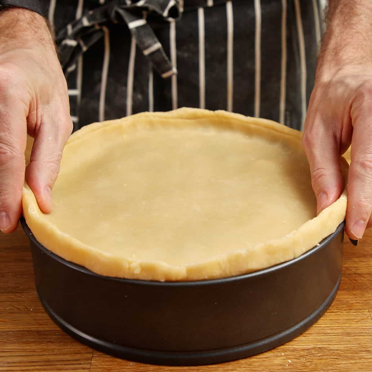 Hands pressing the pastry lid onto a chicken pie to seal it.