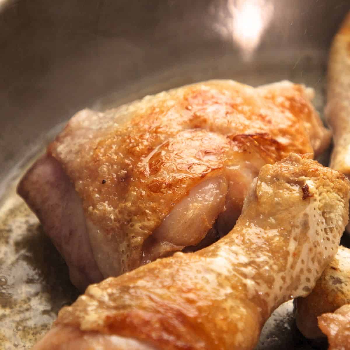 Searing chicken in a stainless steel pan.