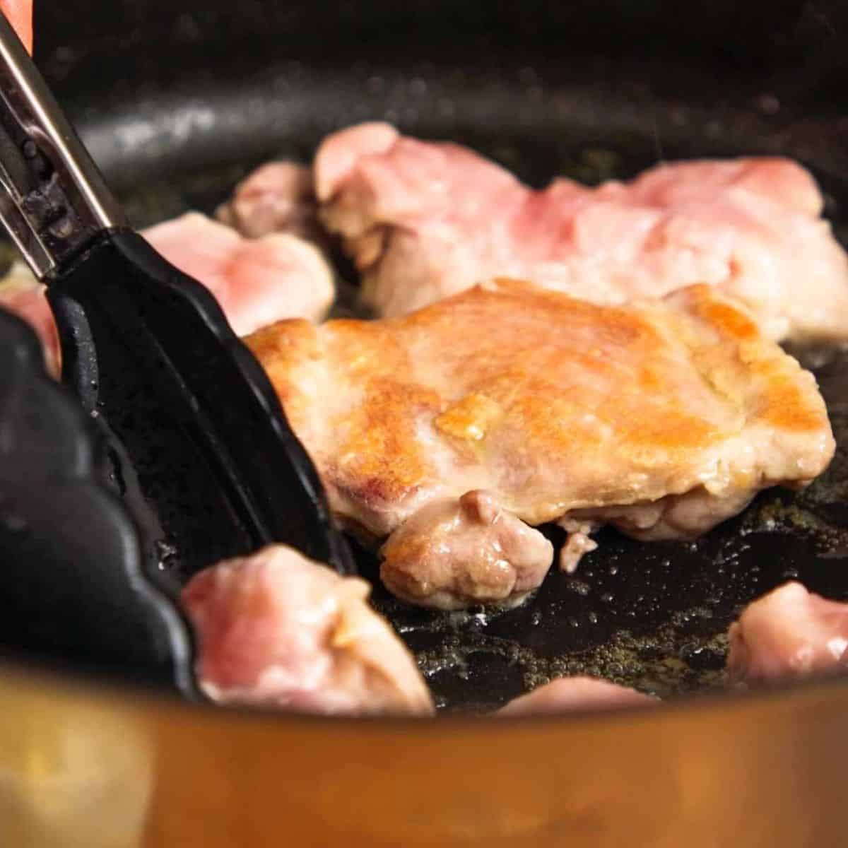 Searing chicken in black pan.