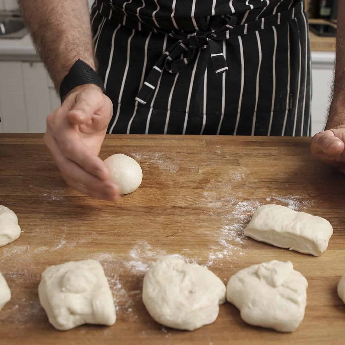 Shaping naan dough balls on wooden surface.