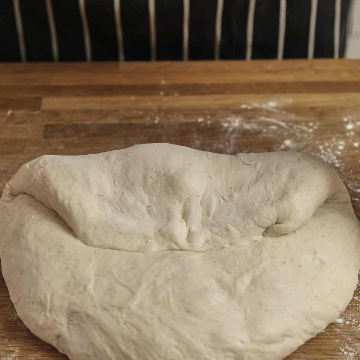 A folded piece of sourdough rests on a floured wooden surface.