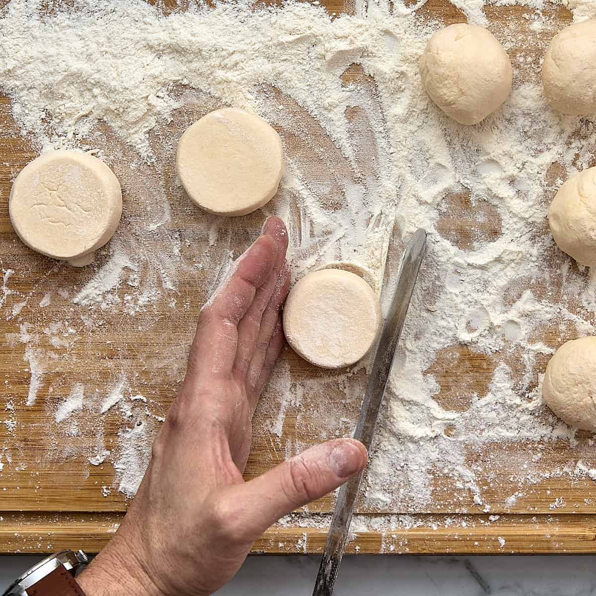 Shaping syrniki(cheese pancakes) with a spatula on a wooden board dusted with flour.