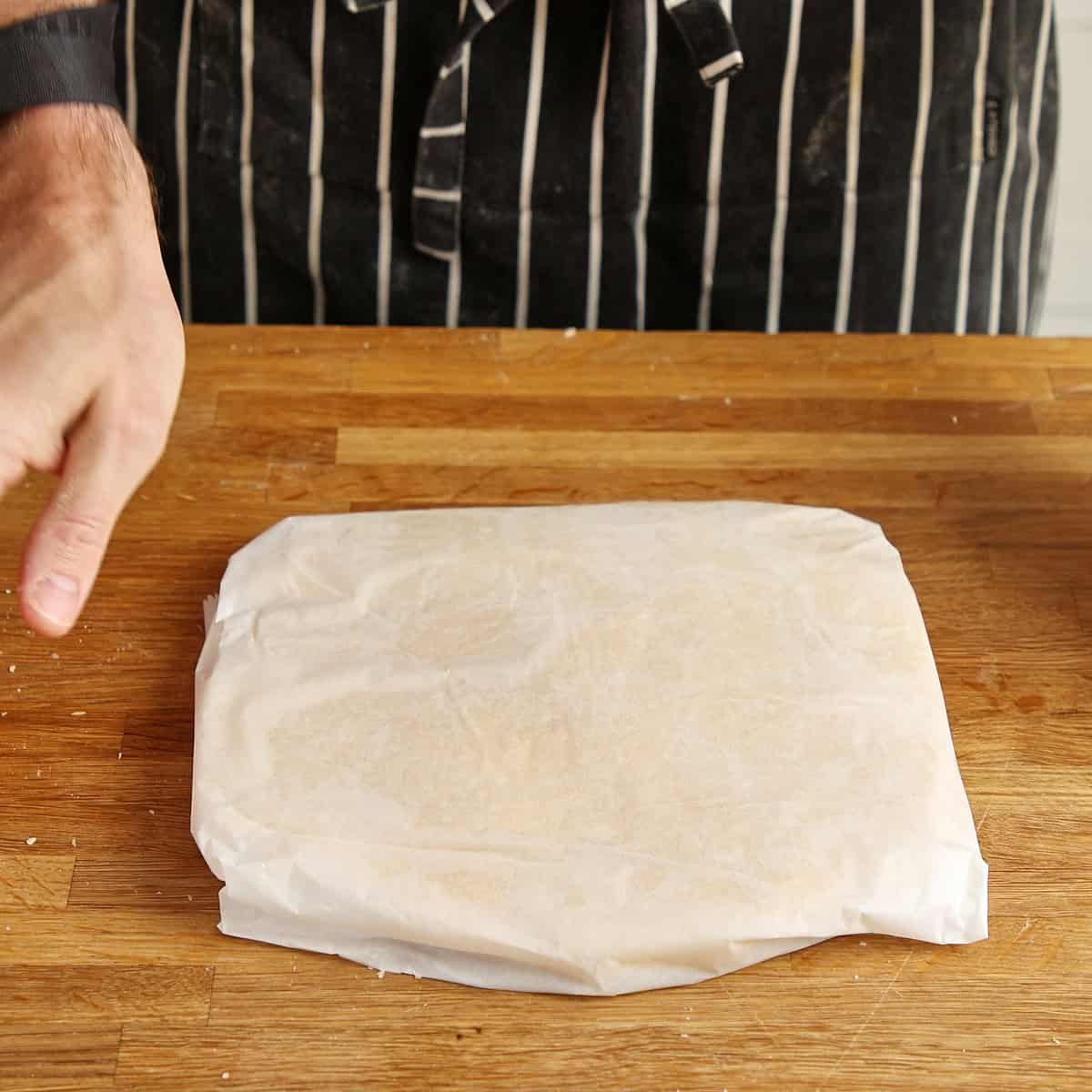 Wrapped shortcrust dough resting on a wooden board.