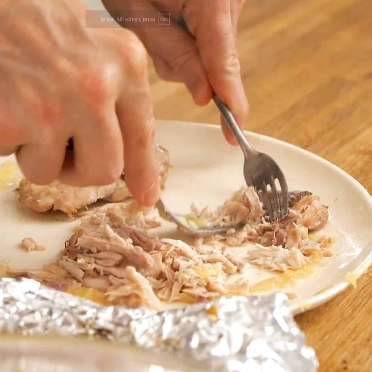 Shredding cooked chicken with a fork for Olivieh salad.