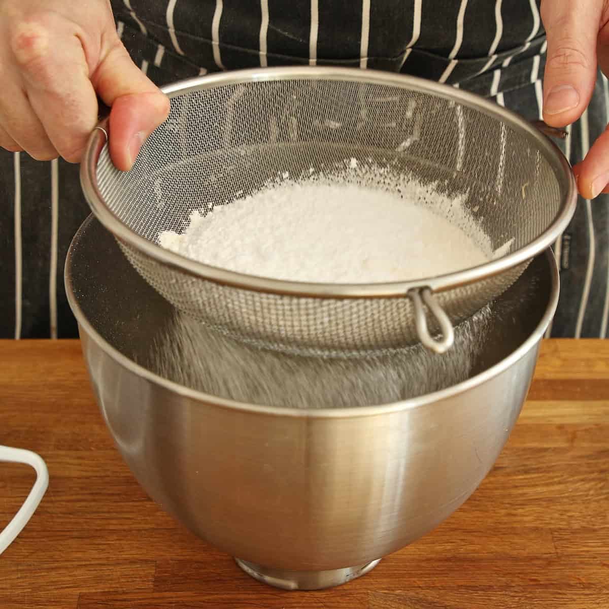 Fine flour sifting through mesh strainer into stainless steel bowl.