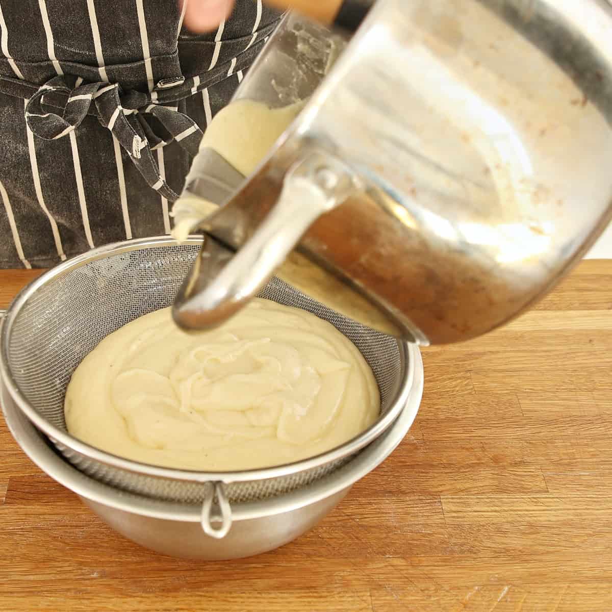 Pale custard filling being strained through fine-mesh sieve into metal bowl.