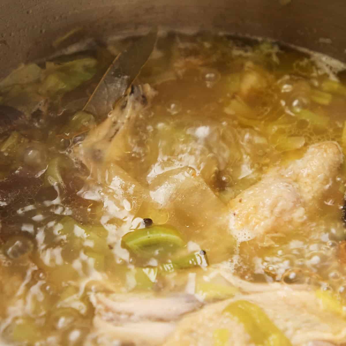 Chicken stock simmering in a stainless steel pot.