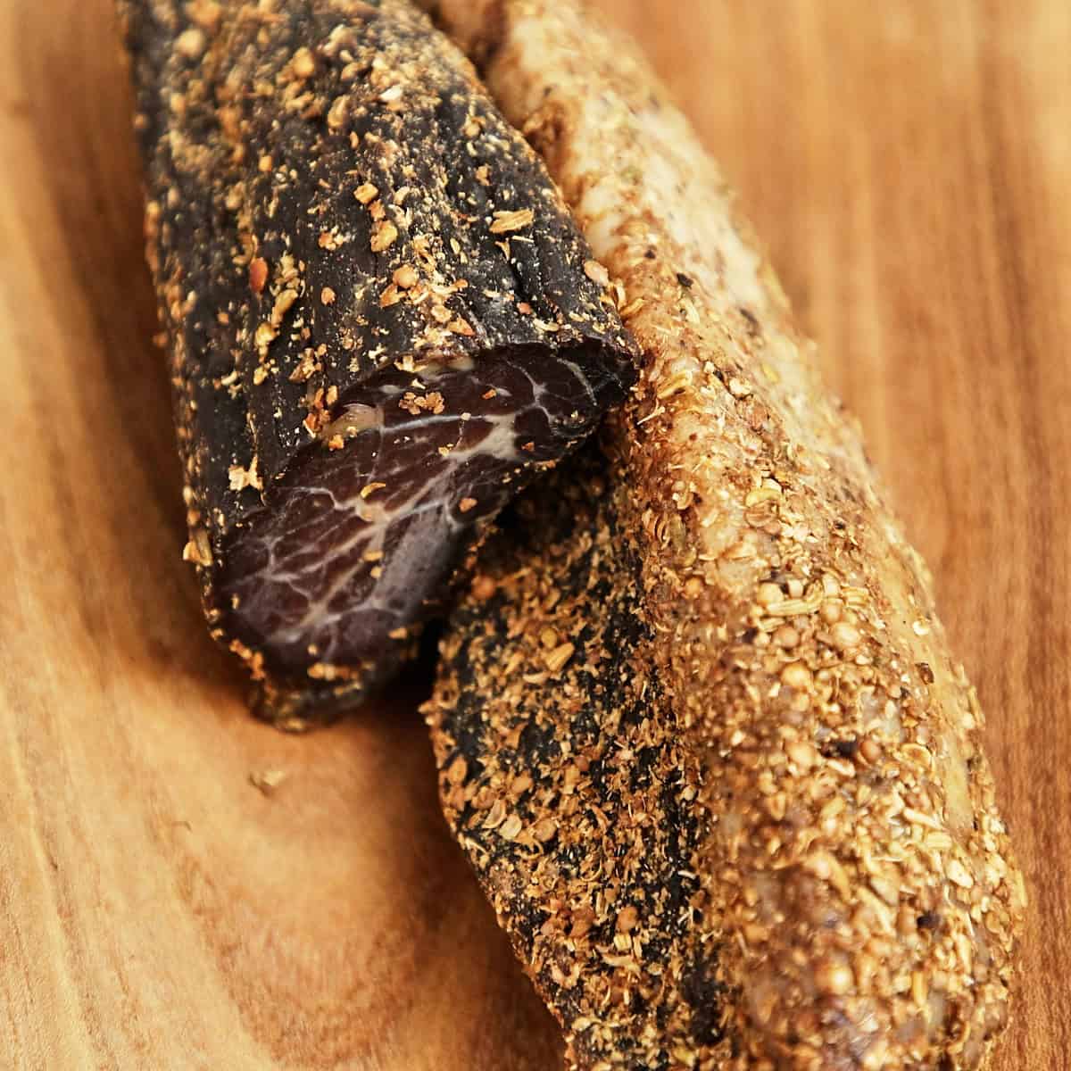 Sliced biltong with visible marbling and spice crust on a wooden cutting board.