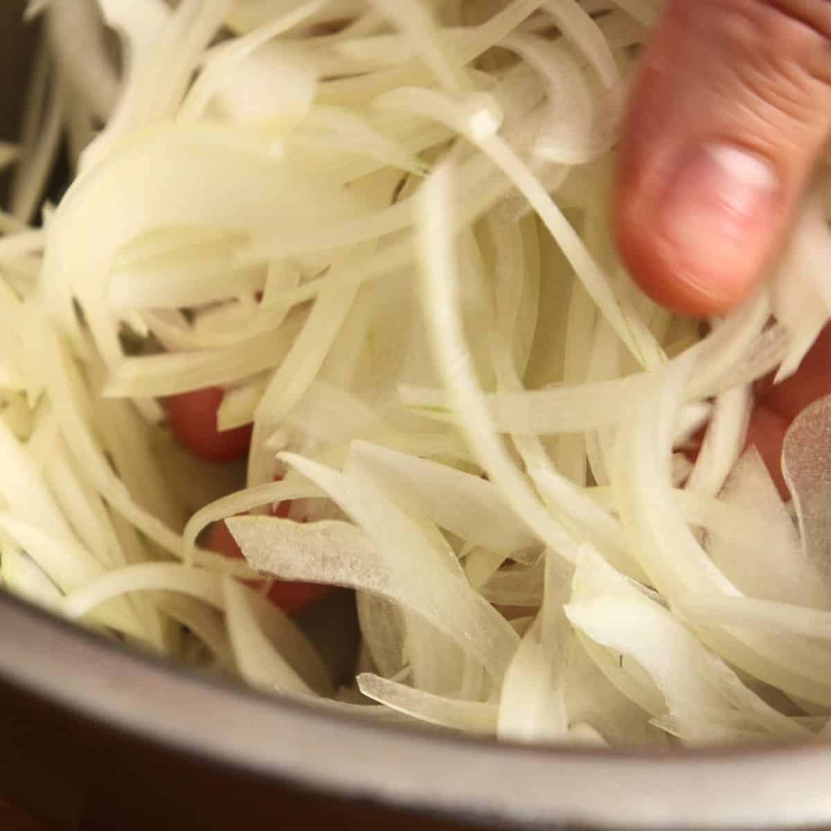 Thinly sliced onions in a metal bowl.