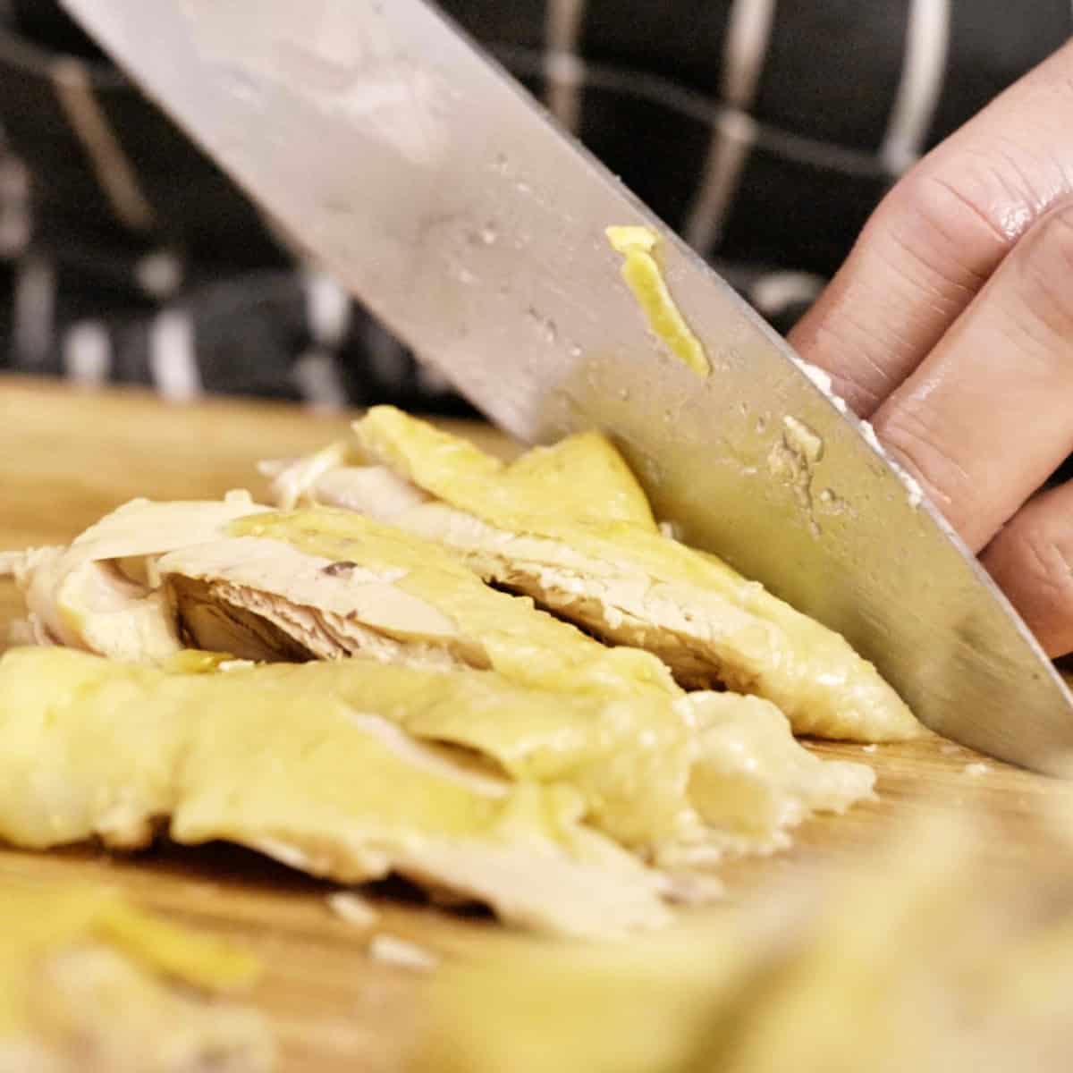 Cutting cooked chicken with a knife on a wooden board.