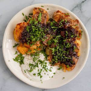 Crispy smashed potatoes with sour cream on a white plate and marble background.