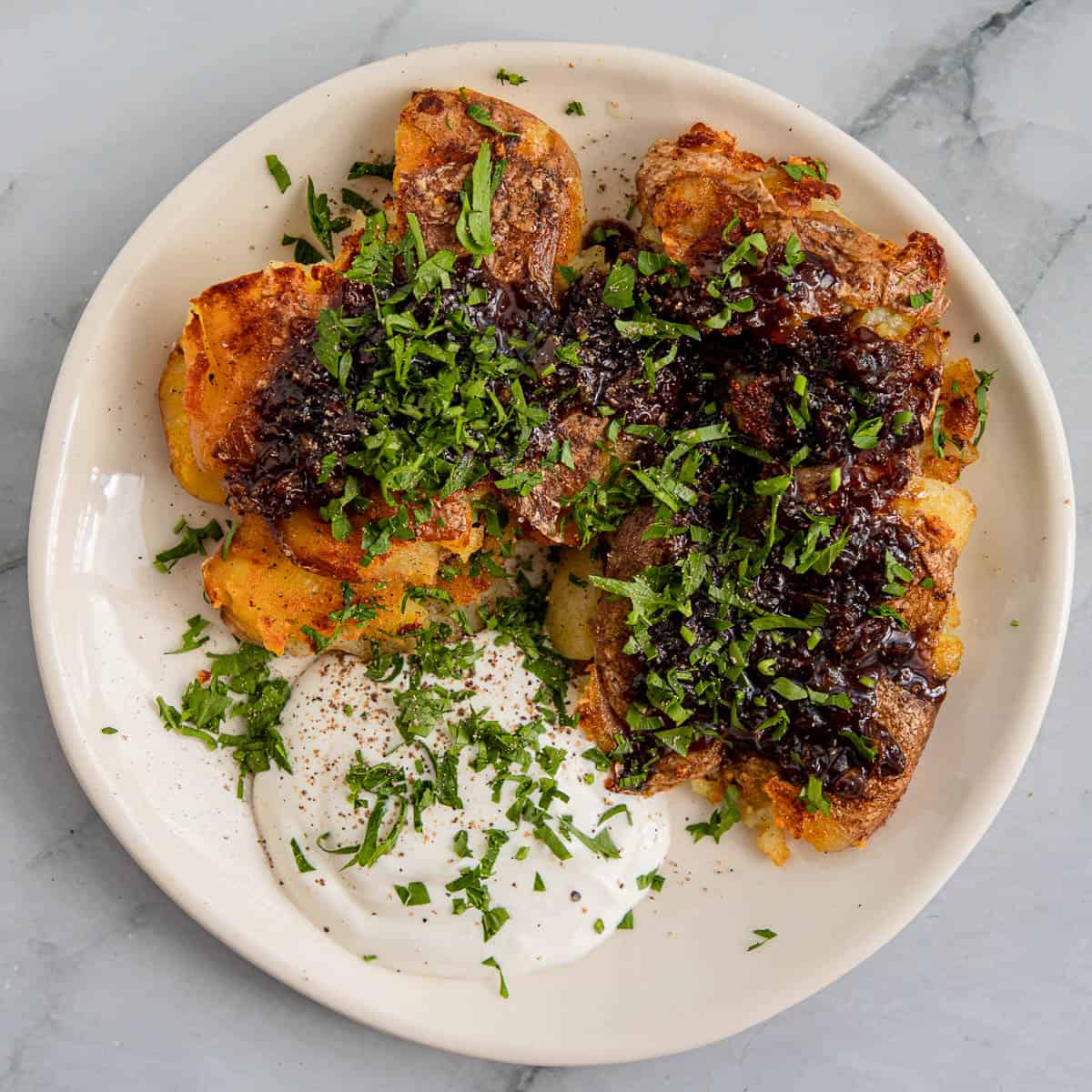 Crispy smashed potatoes with sour cream on a white plate and marble background.