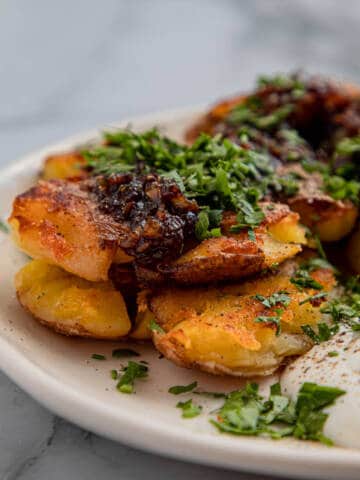 Crispy smashed potatoes with sour cream on a white plate.