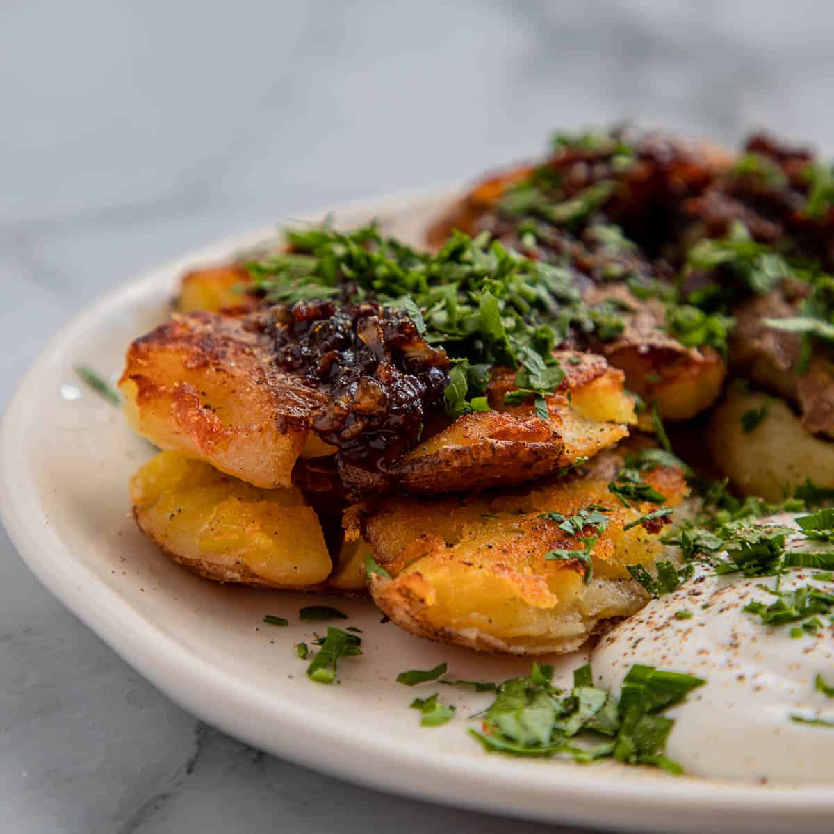 Crispy smashed potatoes with sour cream on a white plate.