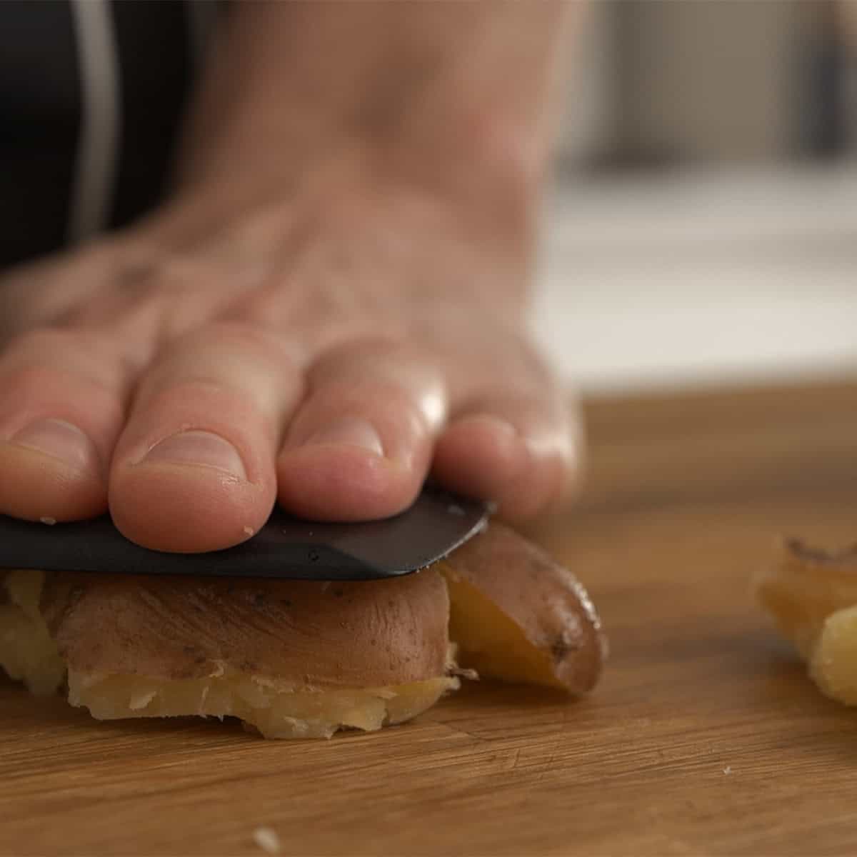 Smashing potatoes on a wooden surface with a spatula.
