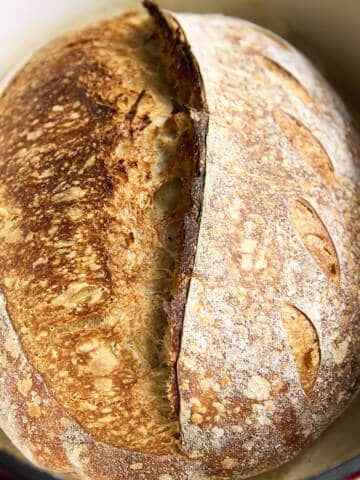 A close-up view of a baked loaf of sourdough bread with a split crust.