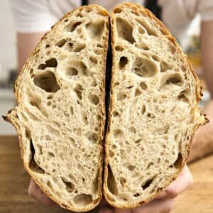 Hands hold two halves of a sliced loaf of sourdough bread to show the airy interior.