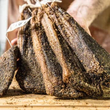 hand holding strips of cured meat on a wooden board