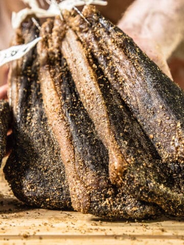 hand holding strips of cured meat on a wooden board